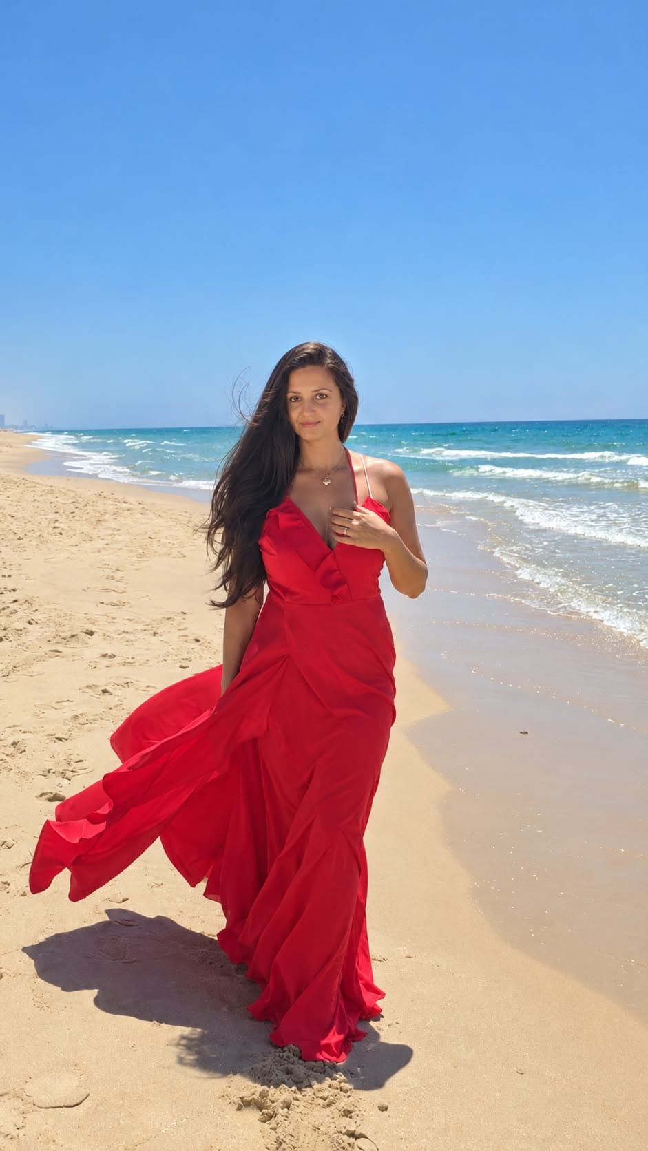 Ruxandra walking on the beach in a red dress, sea and sky around her